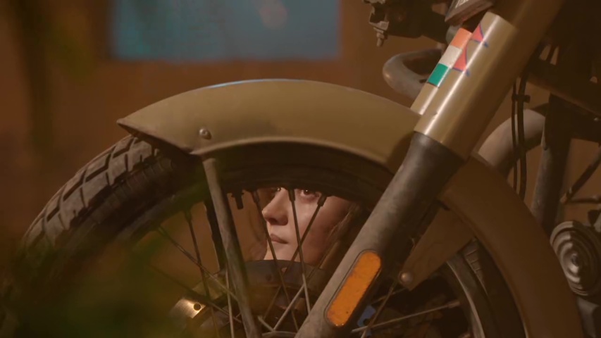 Isha hiding behind bike, looking scared as guards search for her