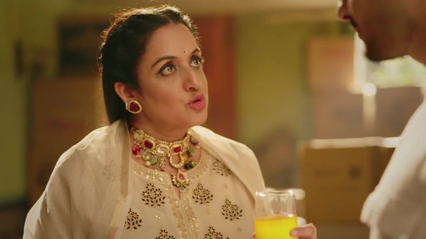 Neetu Aunt holding a glass of juice, looking sneaky, while Mannat watches from behind