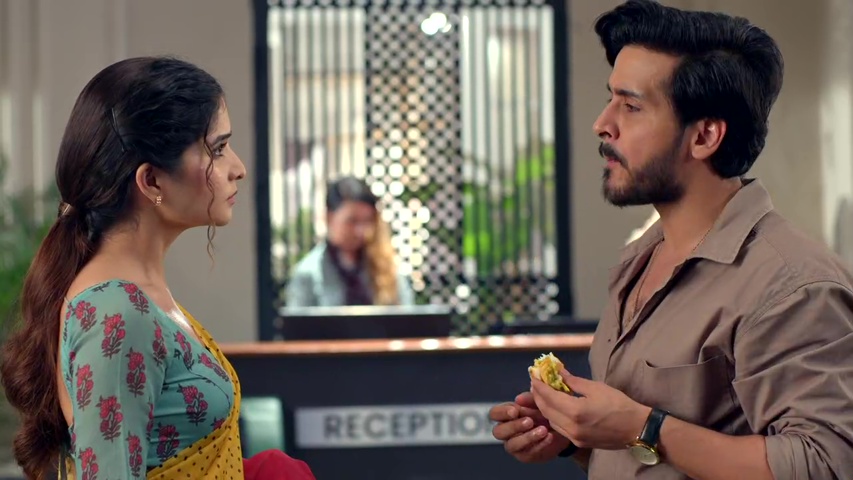 Neil and Savi talking at the hotel, with Neil holding a vada pav